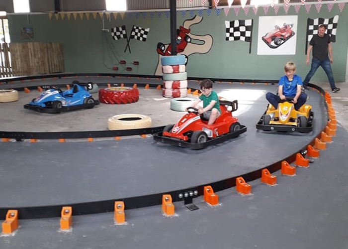 Kids drive go-karts on indoor track with Castleview Open Farm racing decor.
