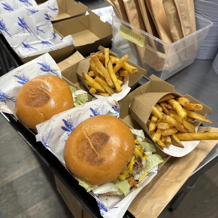 Two burgers and fries in boxes with cutlery packs in the background.