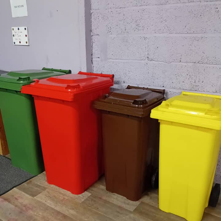 Red, brown, and yellow bins lined up against a textured gray wall.